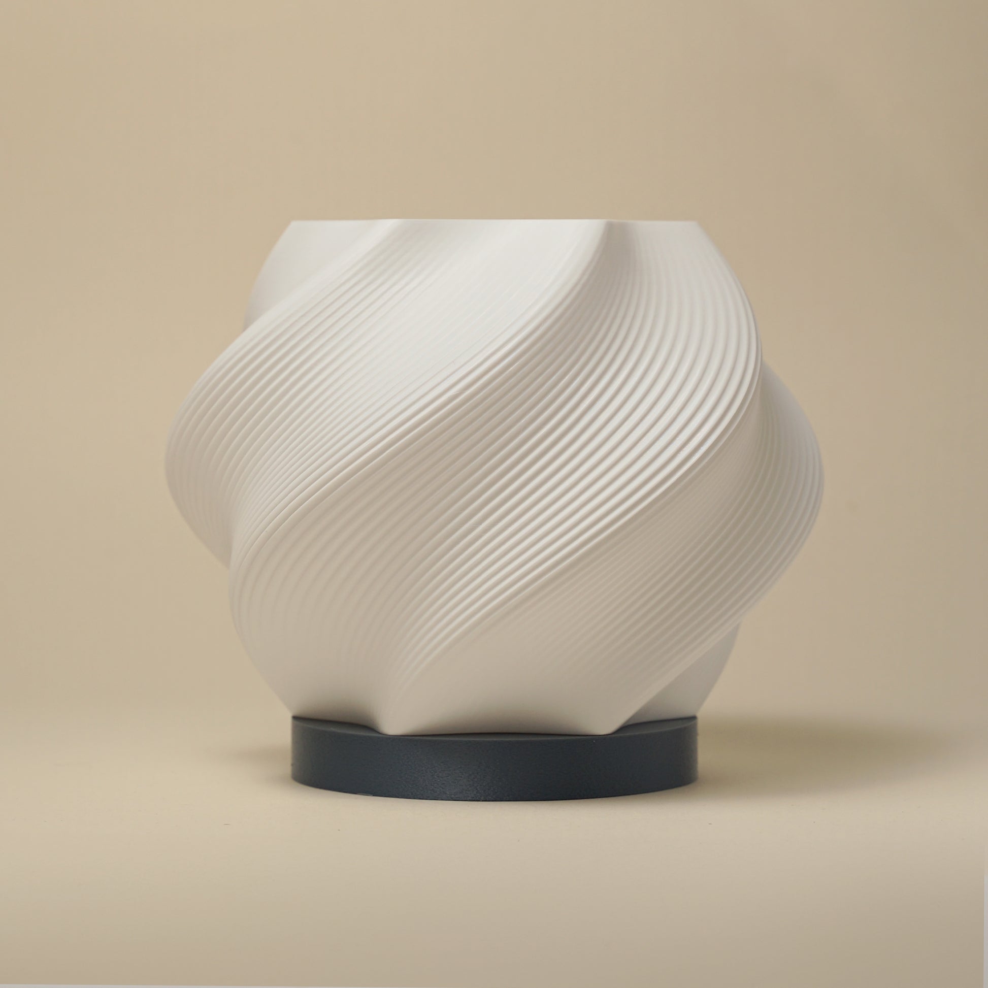 A white 3D-printed lamp with an organic, spiral shape, sitting on a wooden table casting soft, swirling shadows.
